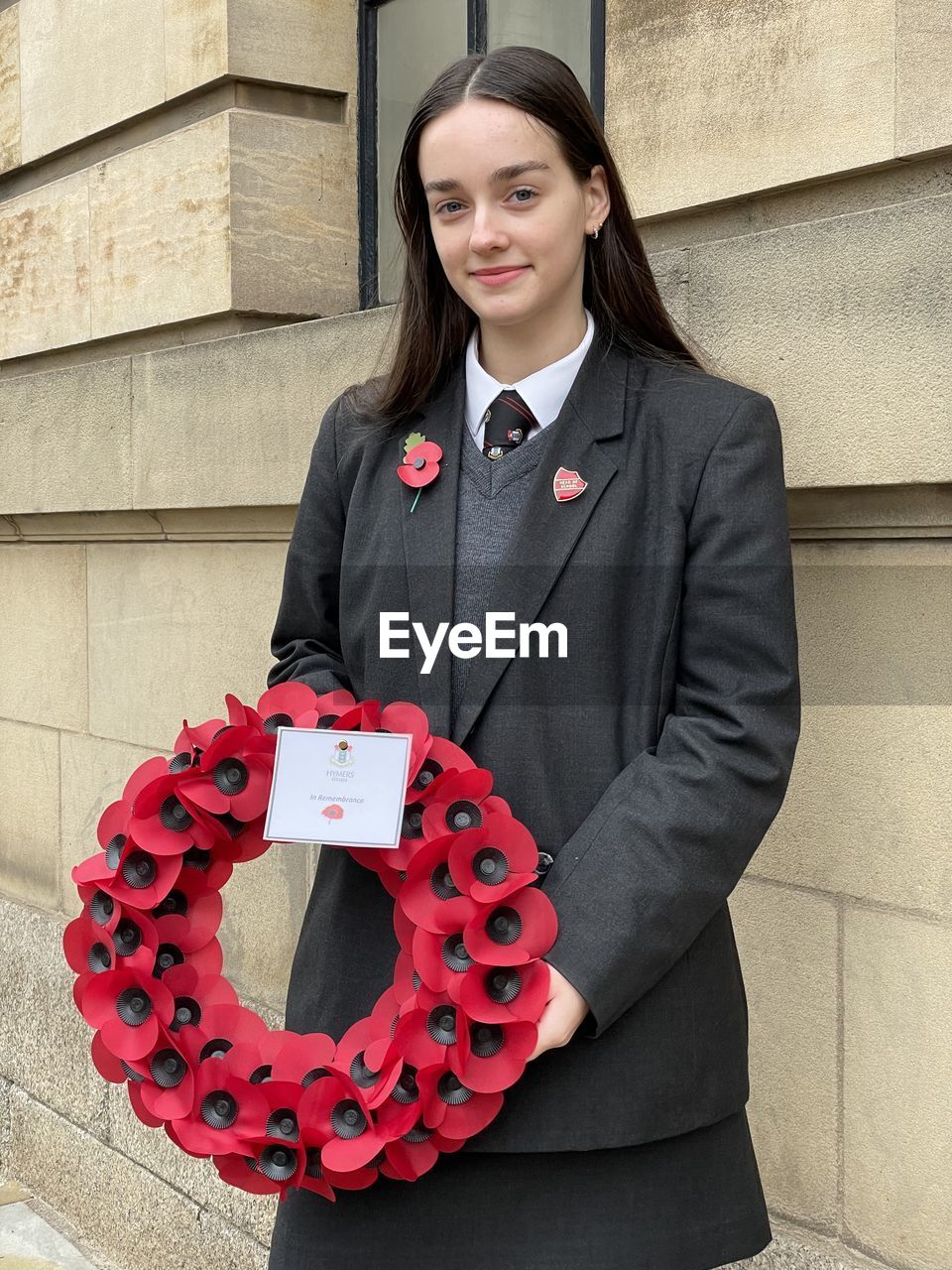 Sixth form girl student in school uniform with poppy wreath to lay at remembrance sunday service 