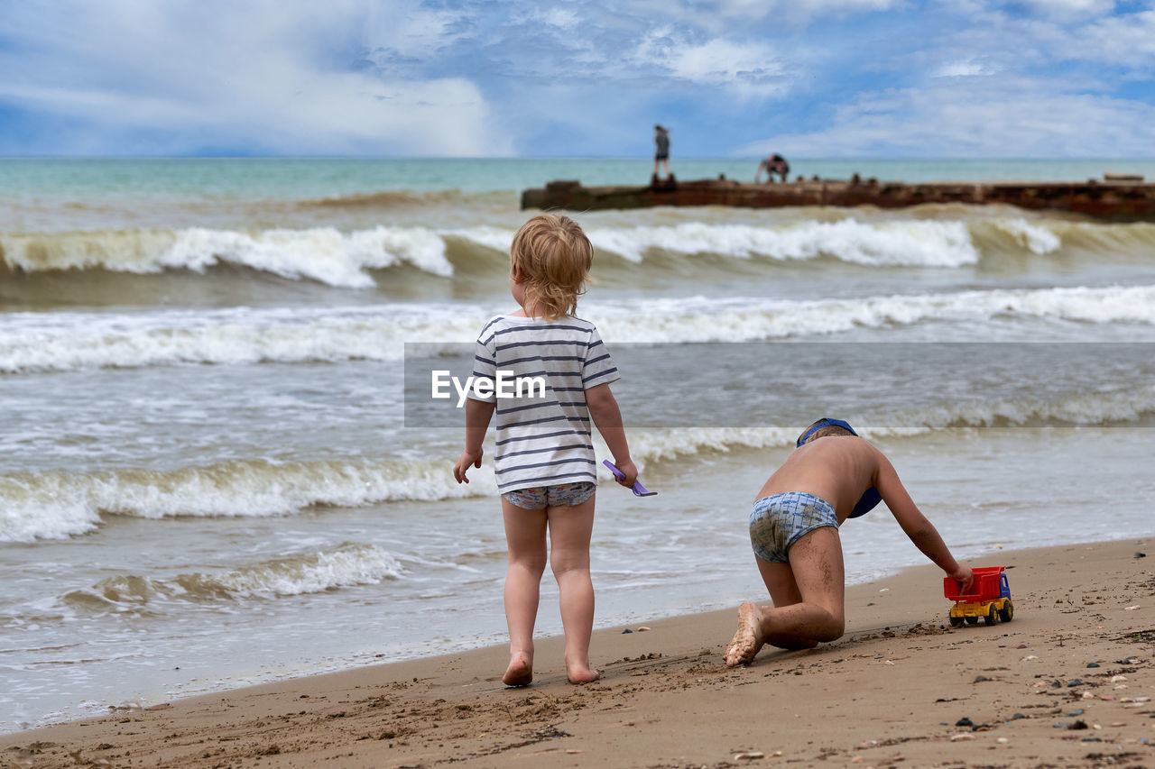 Cute sibling playing on beach against sky