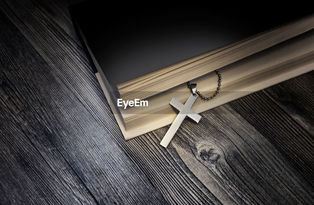 High angle view of cross in book on wooden table