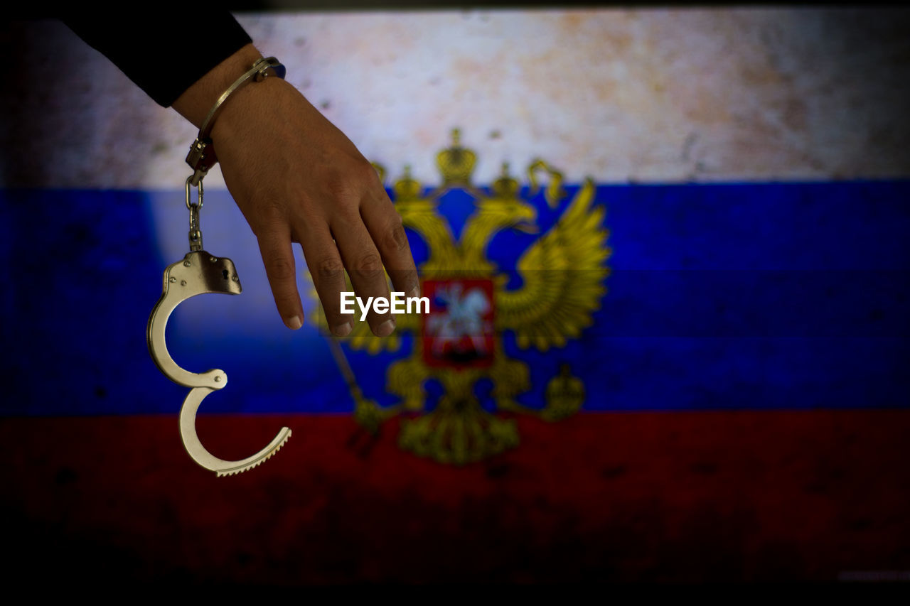 Cropped hand of male criminal with handcuffs against russian flag