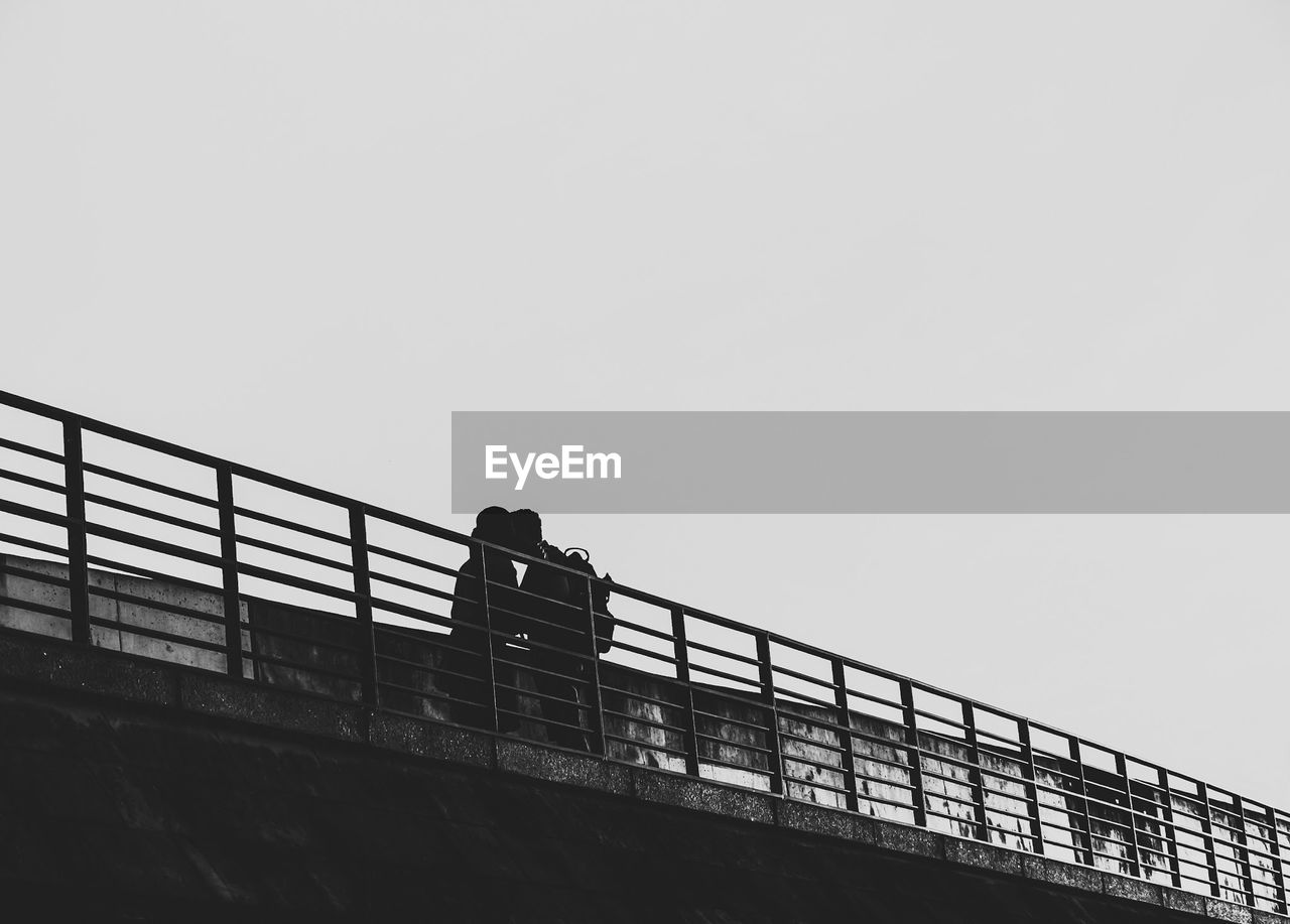 Low angle view of silhouette couple kissing on bridge against clear sky