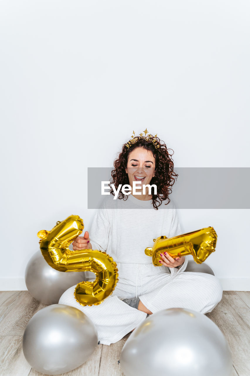 Full length of woman holding balloons sitting on floor against white backgrounds