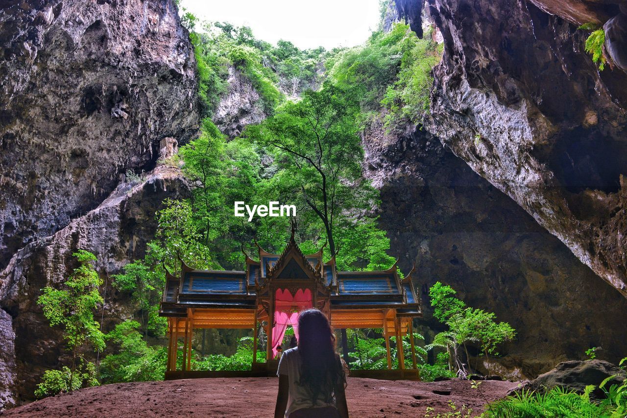 Rear view of woman standing on rock against trees