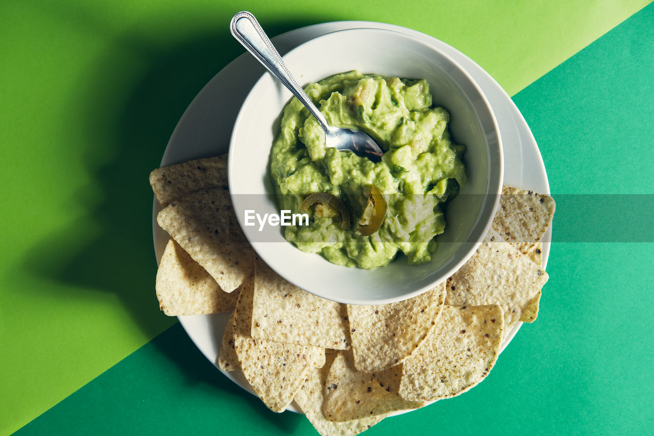 Guacamole sauce in a ceramic bowl on a green background