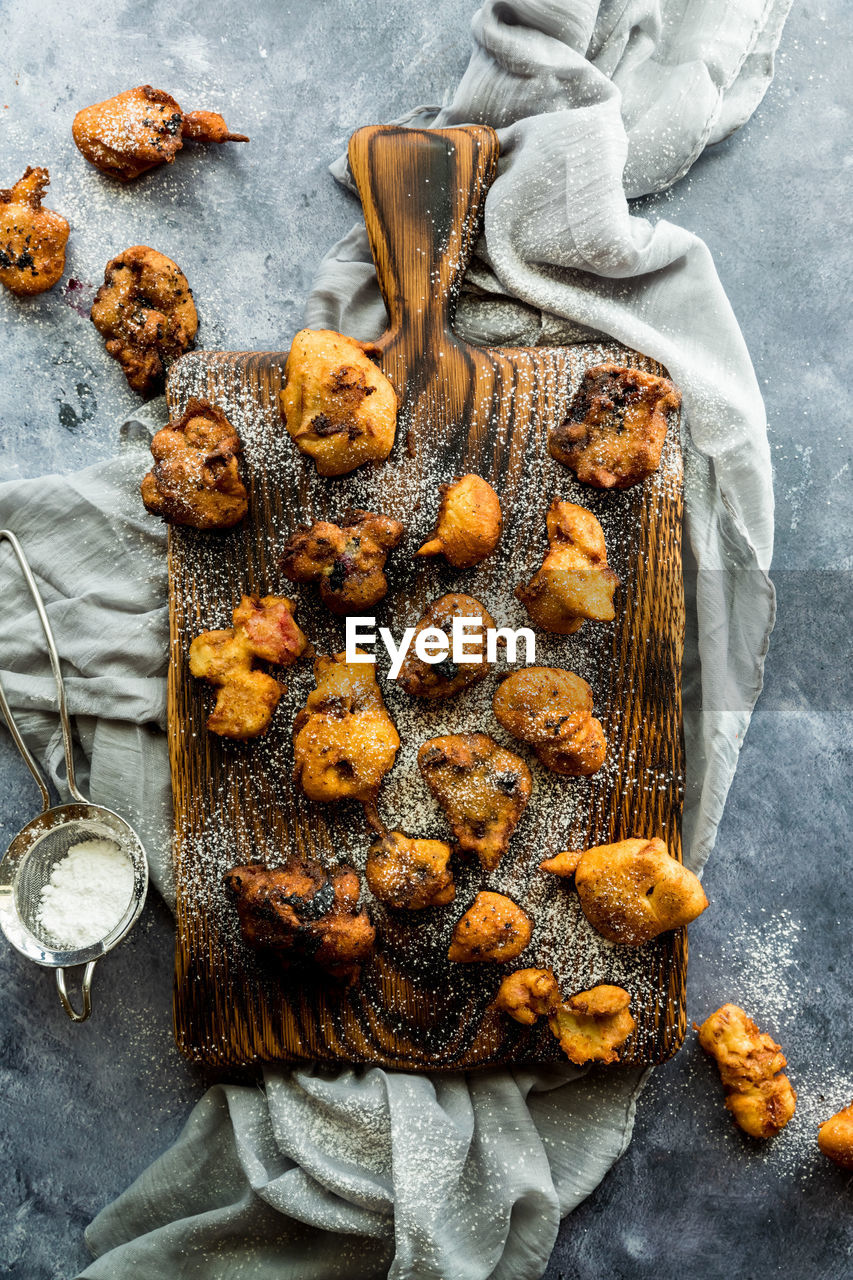 A wooden board topped with fruit filled fritters sprinkled with icing sugar.