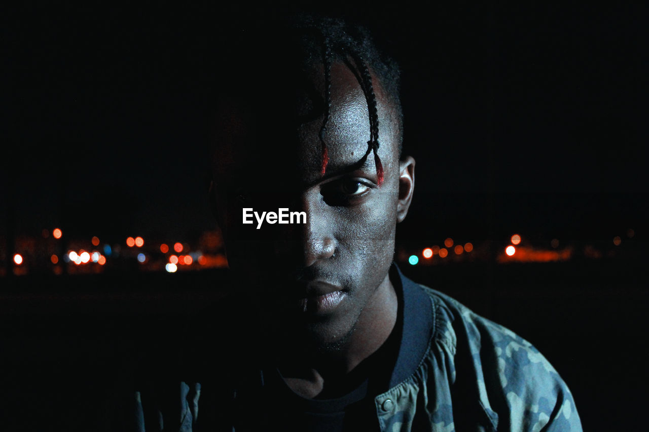CLOSE-UP PORTRAIT OF YOUNG MAN WITH ILLUMINATED LIGHTING EQUIPMENT