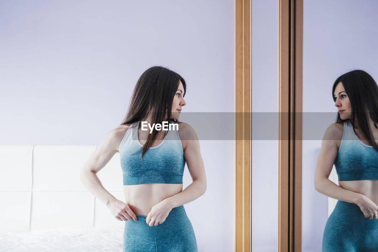 Sportswoman standing and looking in mirror at home