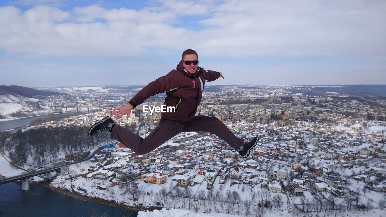 Full length of man jumping on snow against cityscape and sky