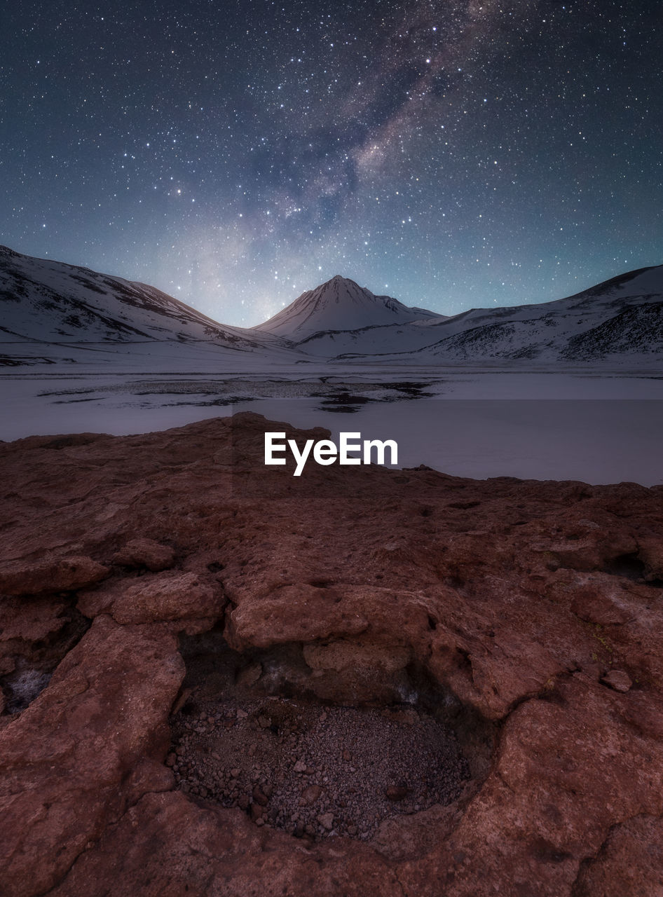 Scenic view of frozen lake by mountain against sky at night