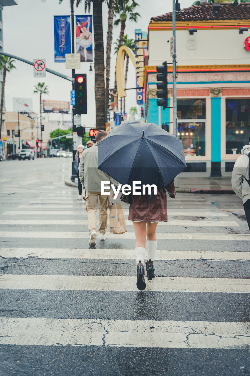 Fashionable young woman walks down a rainy street with a plain black umbrella, skirt and boots.