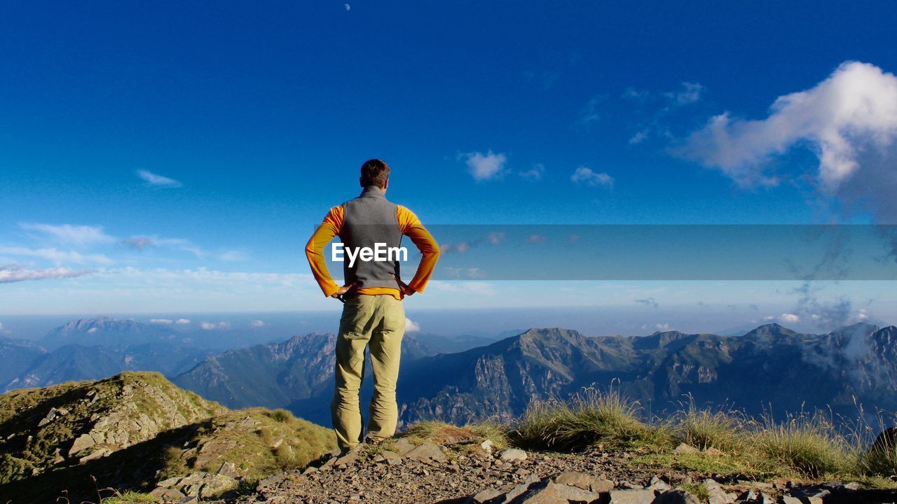 Rear view of man standing on mountain peak against blue sky