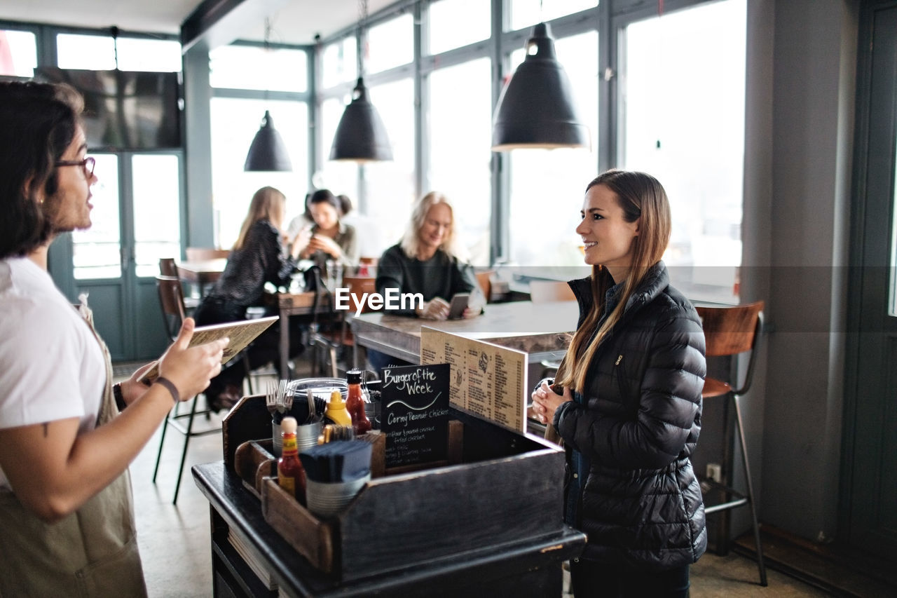 Owner talking to smiling young customer while standing in lectern