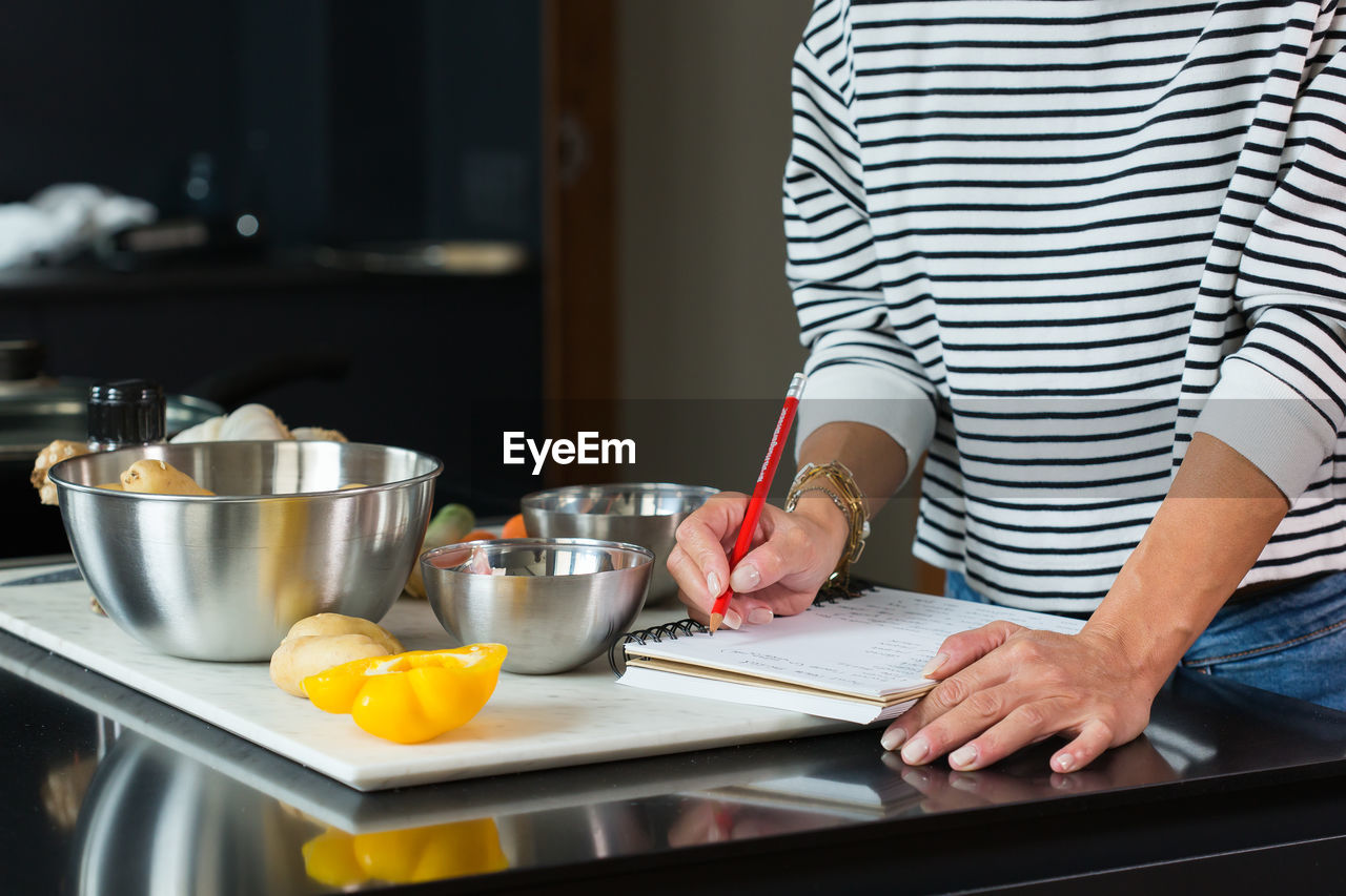 Woman checking recipe and ingredients in her notebook while cooking pie in the modern kitchen