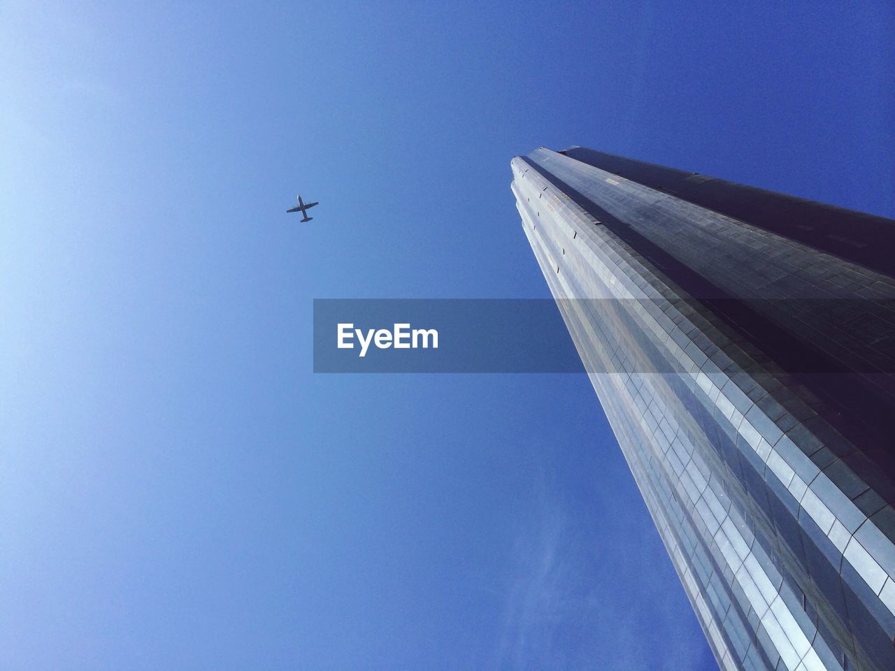 Low angle view of world trade center against airplane flying in blue sky