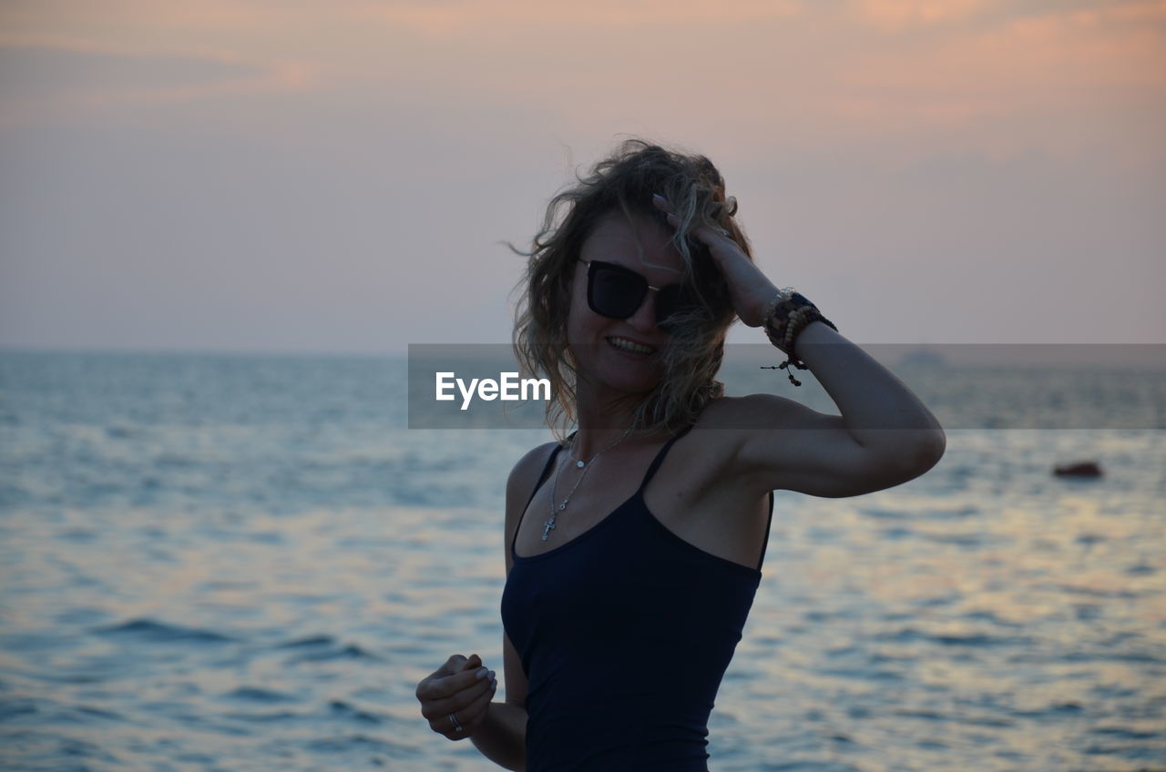 Young woman wearing sunglasses standing at beach during sunset