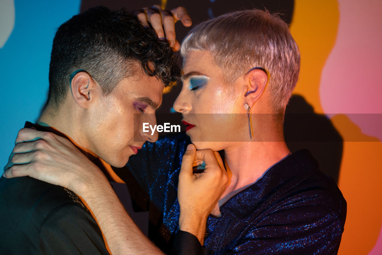 Portrait of gay couple wearing makeup and embracing in illuminated studio