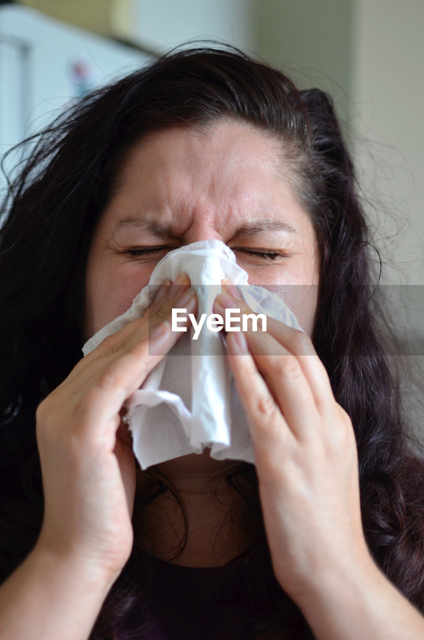 Close-up of woman sneezing at home