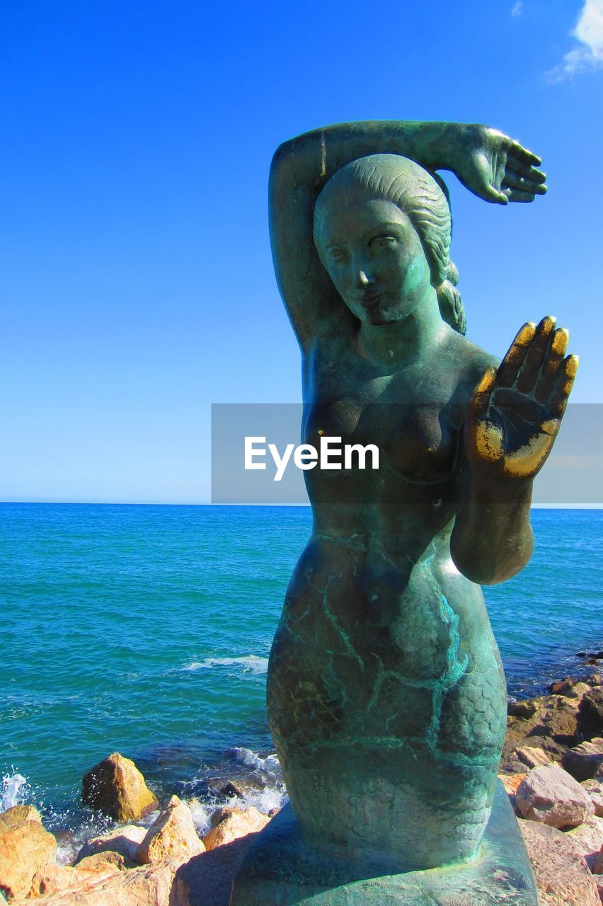 Nude female statue on beach against blue sky