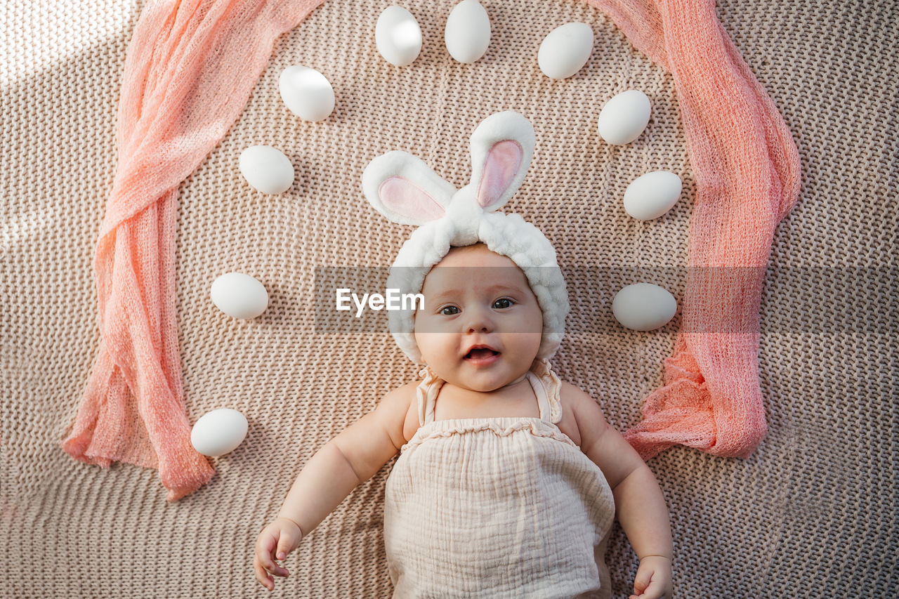 Newborn baby lies on a bed in pastel colors like an easter bunny on the grass with eggs