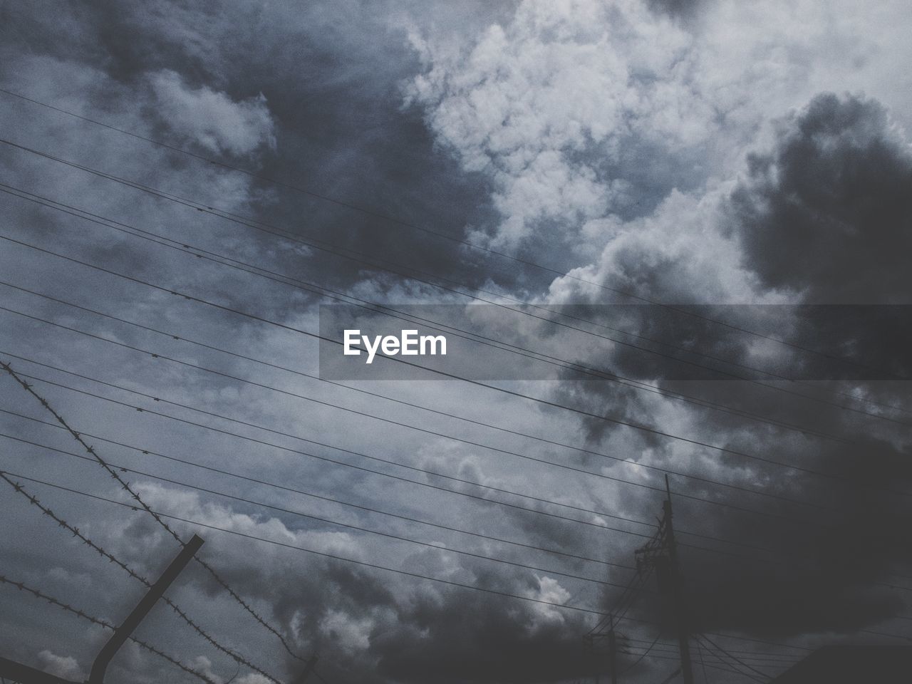 Low angle view of power lines against cloudy sky