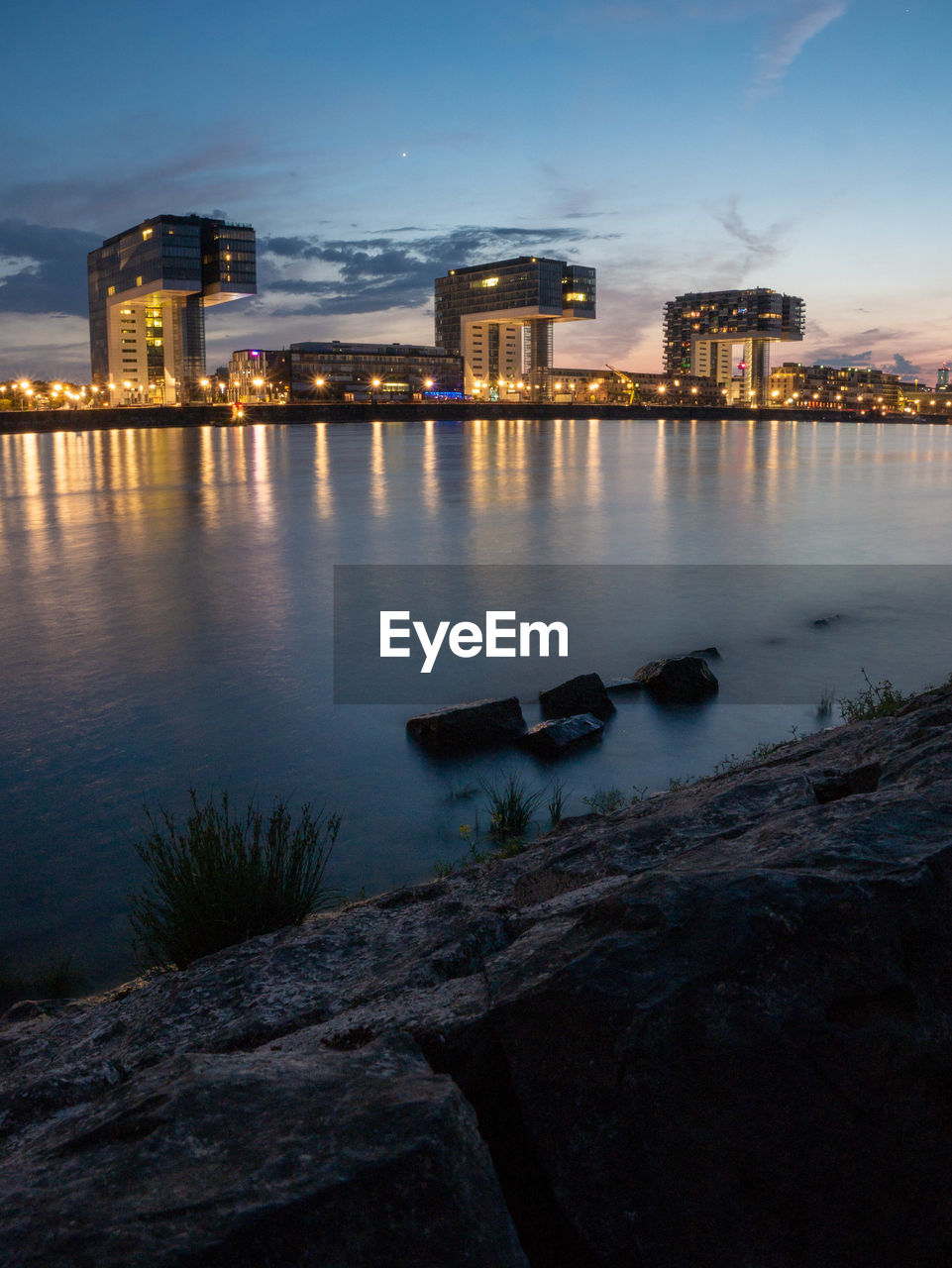 RIVER BY ILLUMINATED BUILDINGS AGAINST SKY AT DUSK