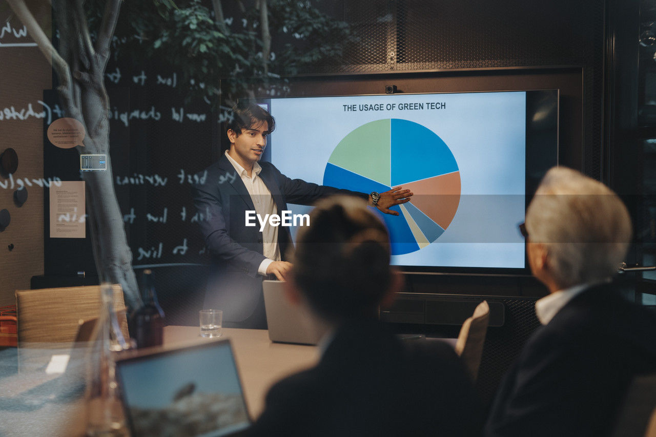 Young businessman explaining pie chart to male and female colleagues during business meeting