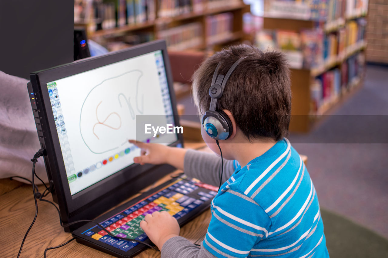 A child with head phones works an interactive game on a laptop at the library