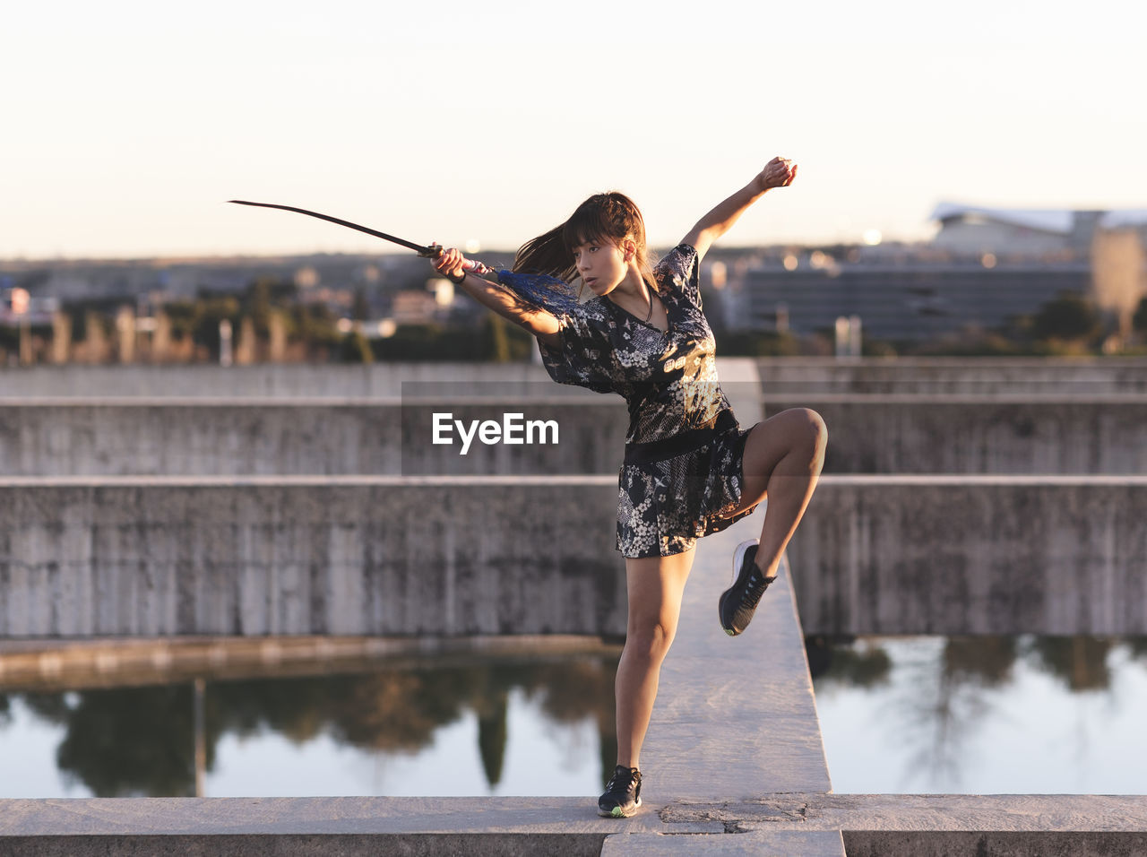 Female athlete practicing sword on structure against clear sky at sunset