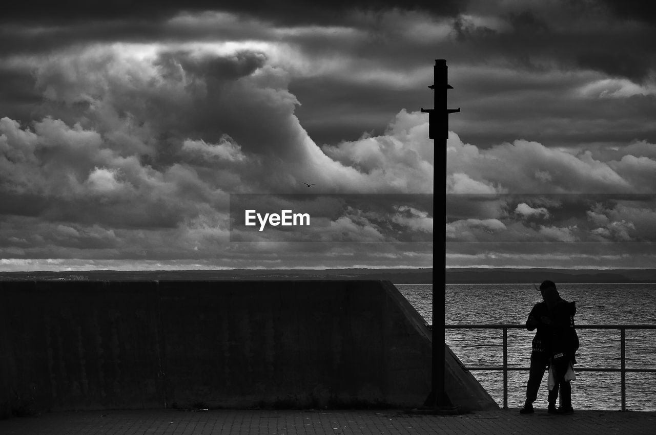 MAN STANDING ON SEA SHORE AGAINST SKY