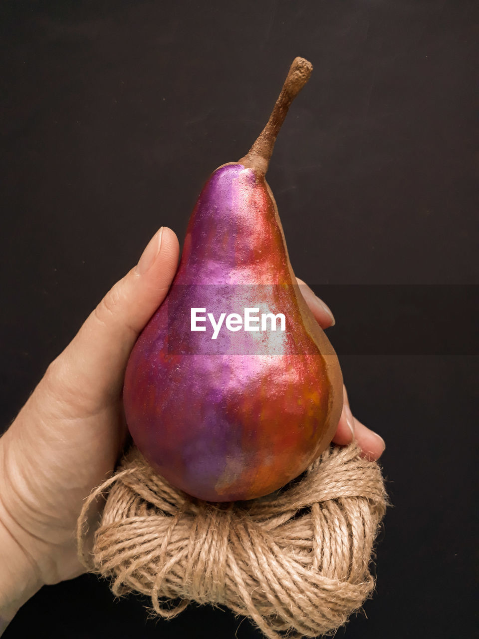 Close-up of person holding pear with rope against black background