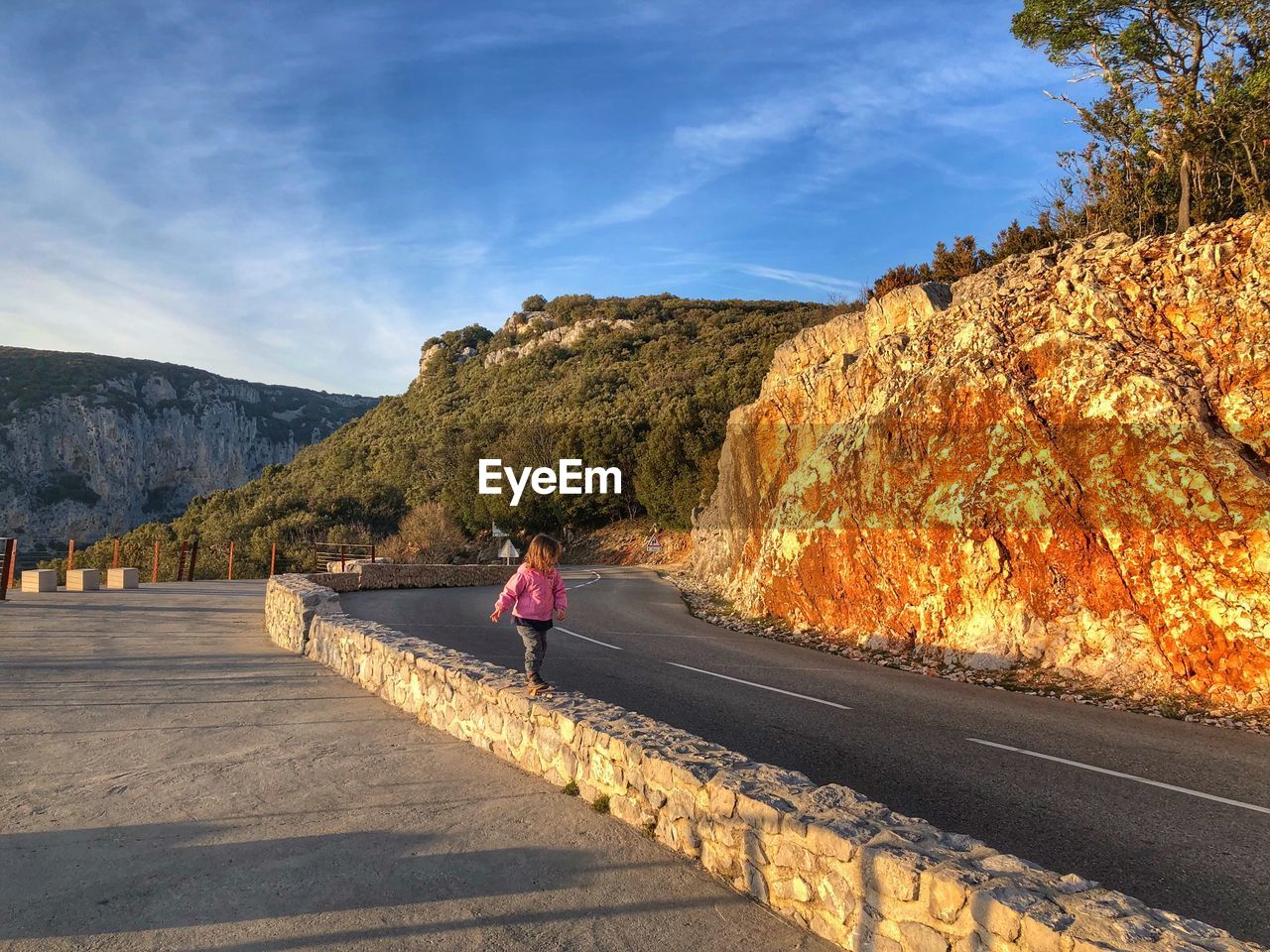 Girl walking on retaining wall against blue sky