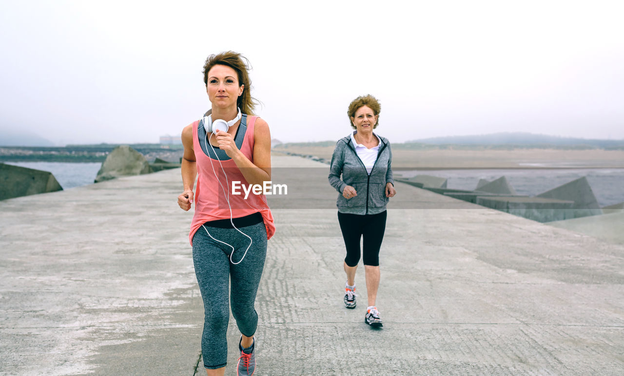 Woman with mother jogging on pier against sky