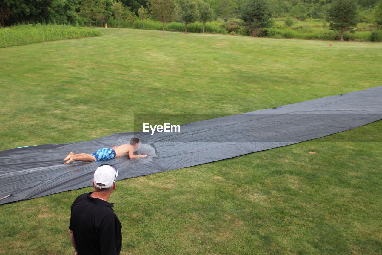 REAR VIEW OF MAN WITH UMBRELLA ON GRASS