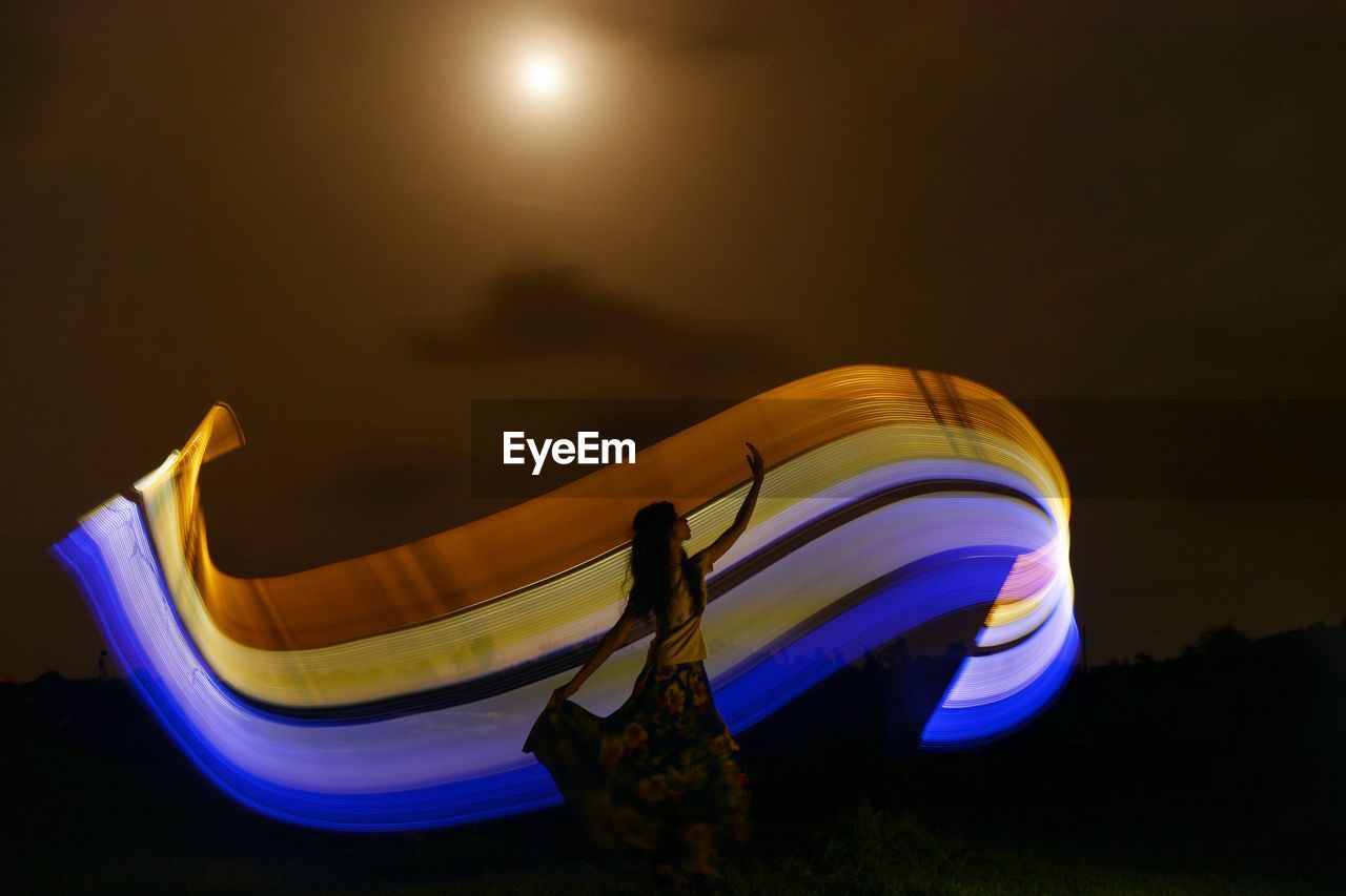 Woman standing by light painting against sky at night