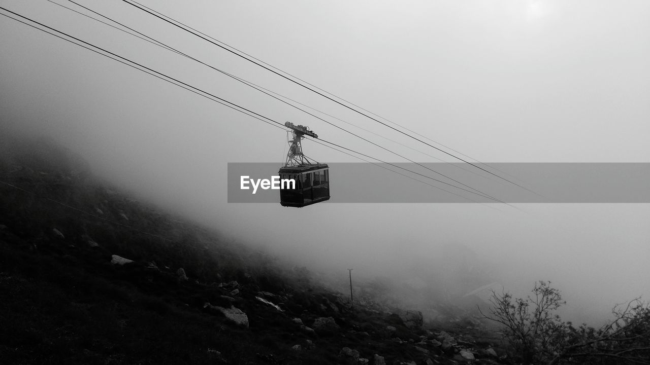 Low angle view of overhead cable car against sky during foggy weather