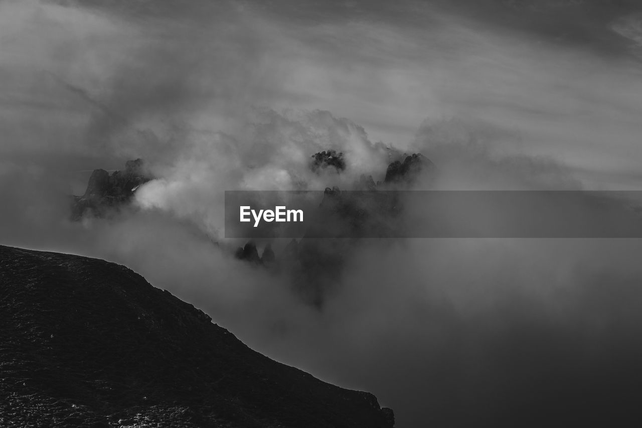 Dramatic black and white effect of dolomite peaks half hidden by clouds and fog,