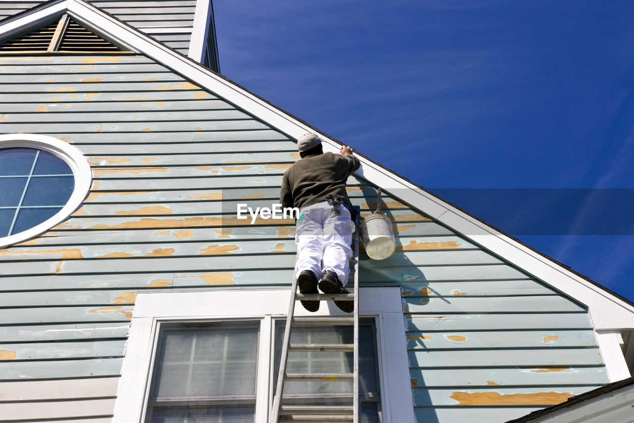 Low angle view of man painting house while standing on ladder