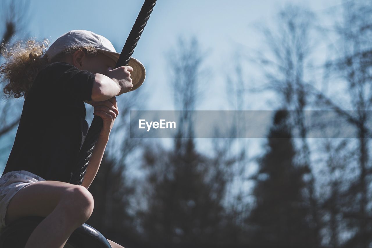 Low angle view of girl swinging on tire swing against sky