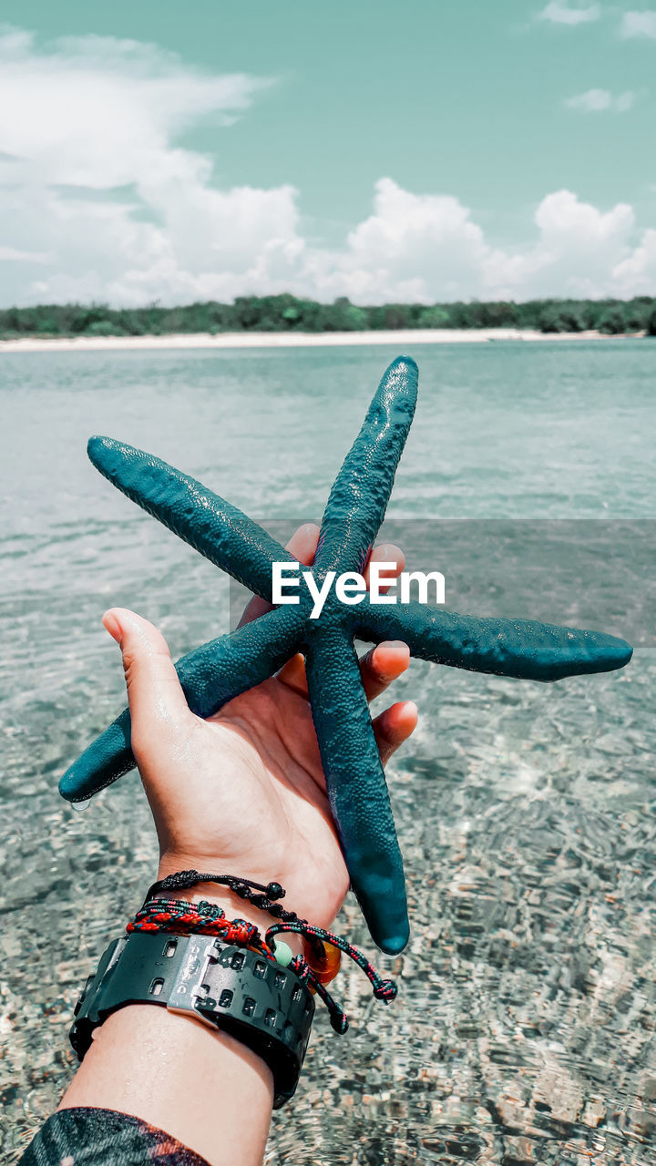 Cropped hand of woman holding star fish against sky