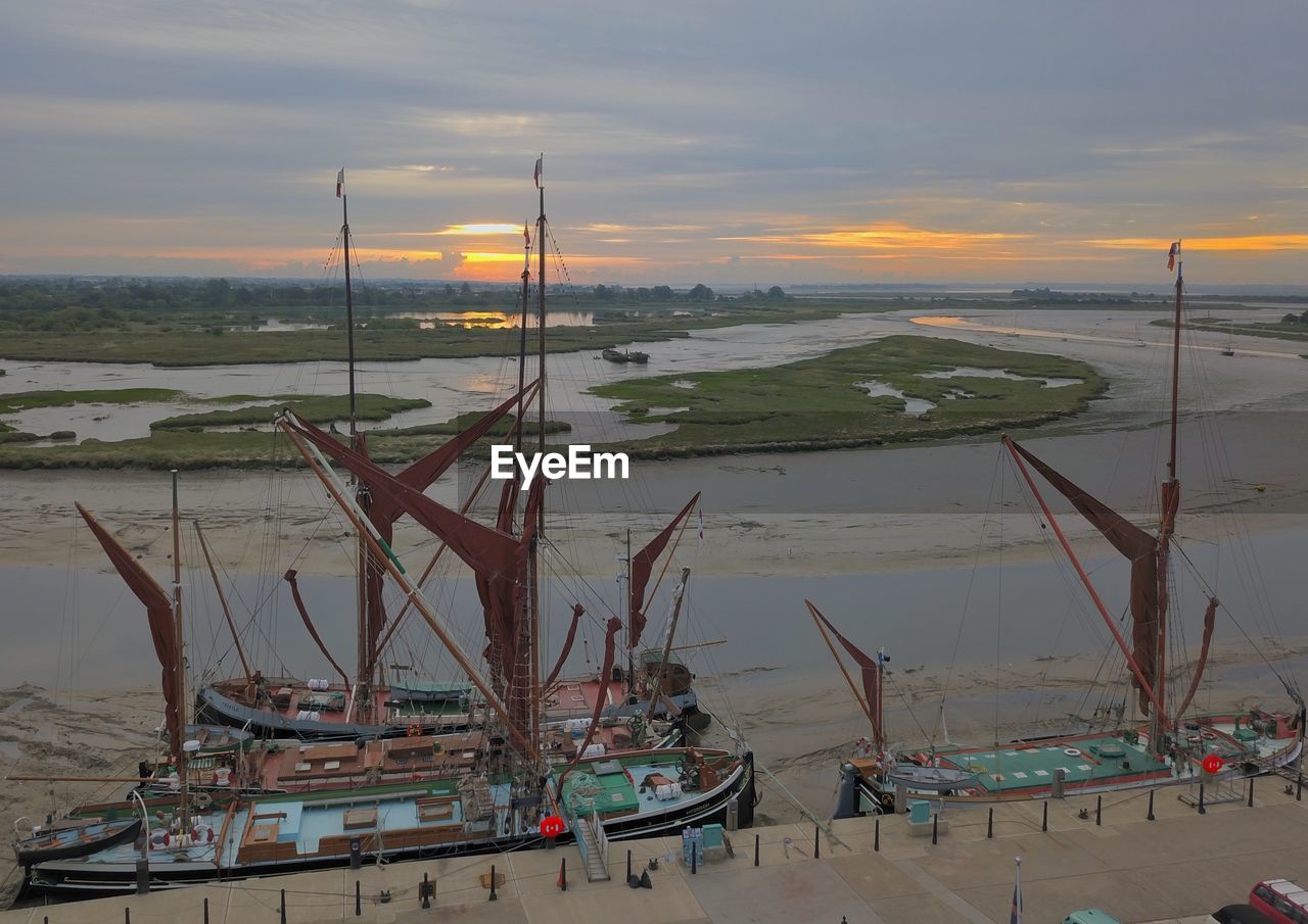 Sailboats moored on sea against sky during sunset