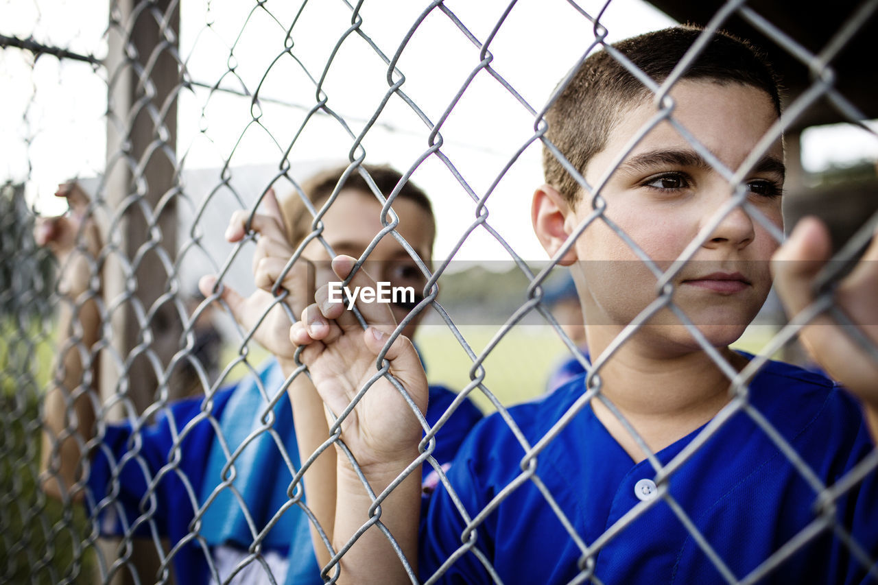 Boy looking through fence while standing in dugout