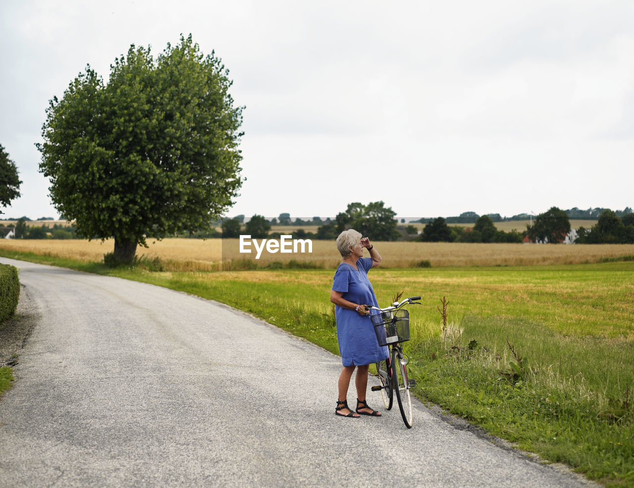 Elderly woman with bicycle by field