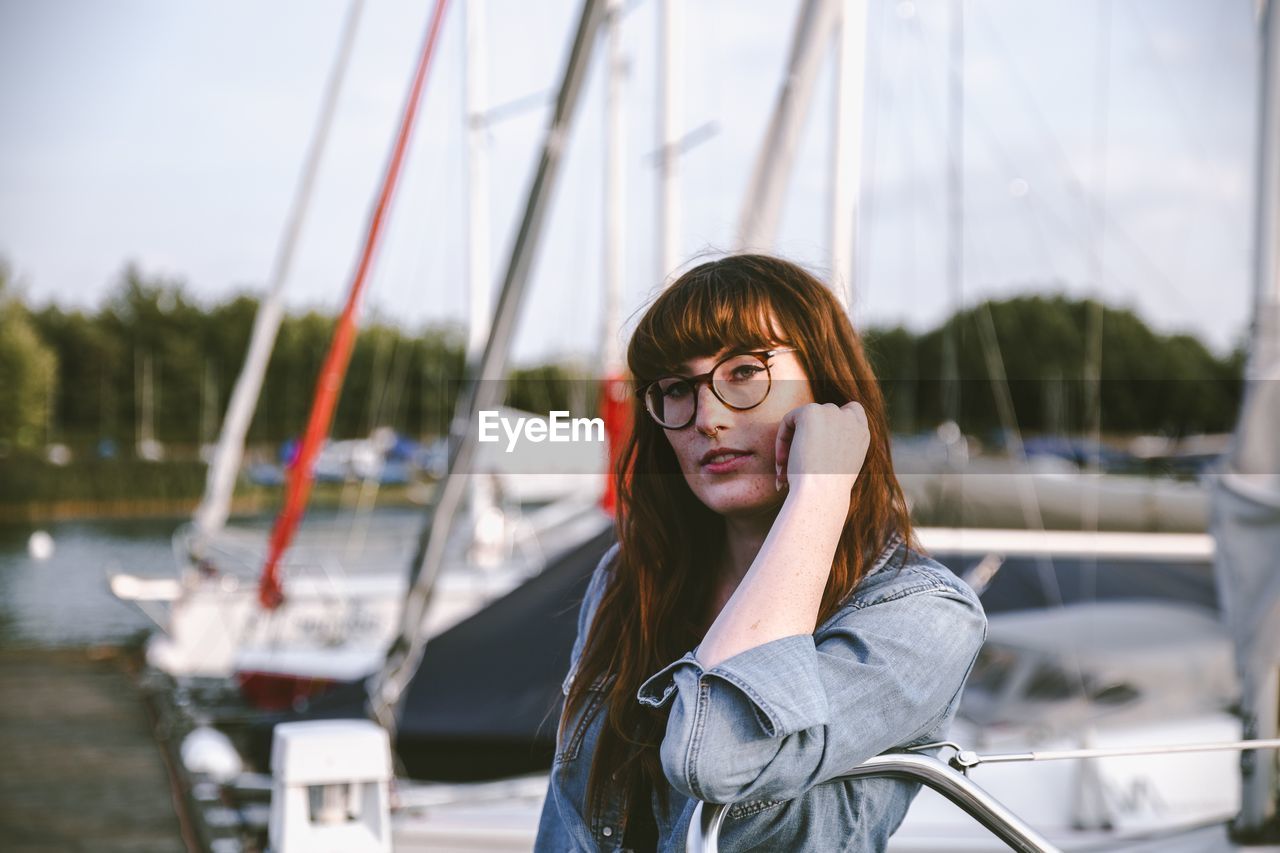 PORTRAIT OF YOUNG WOMAN IN SUNGLASSES AGAINST BOAT
