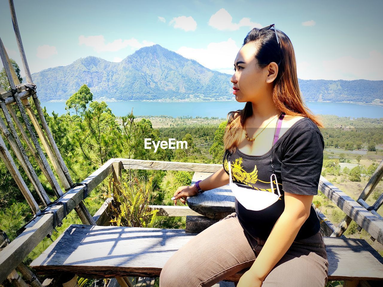 BEAUTIFUL YOUNG WOMAN SITTING ON SEAT AGAINST MOUNTAINS