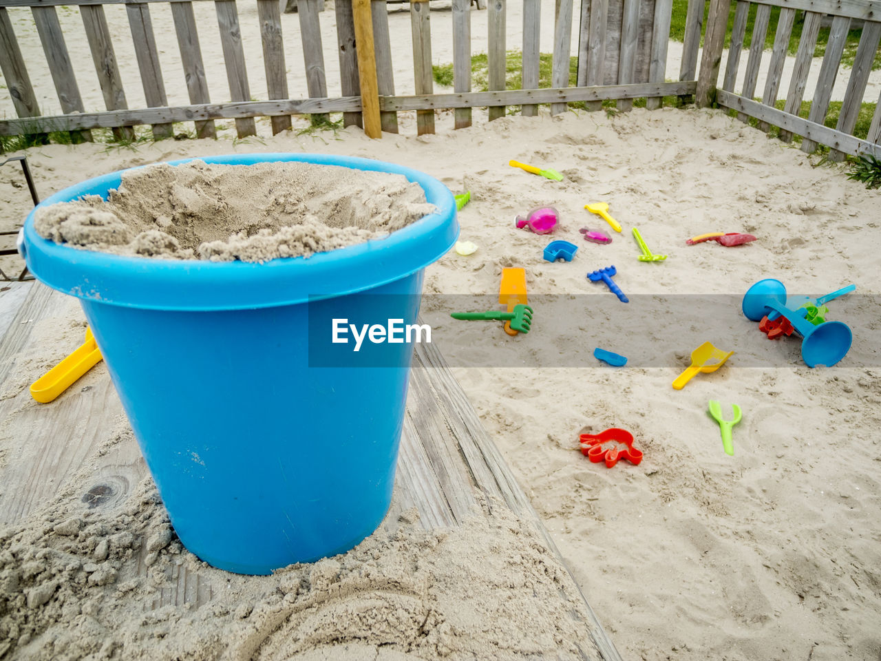 Fenced sandpit on the german north sea coast with blue sand bucket in the foreground.