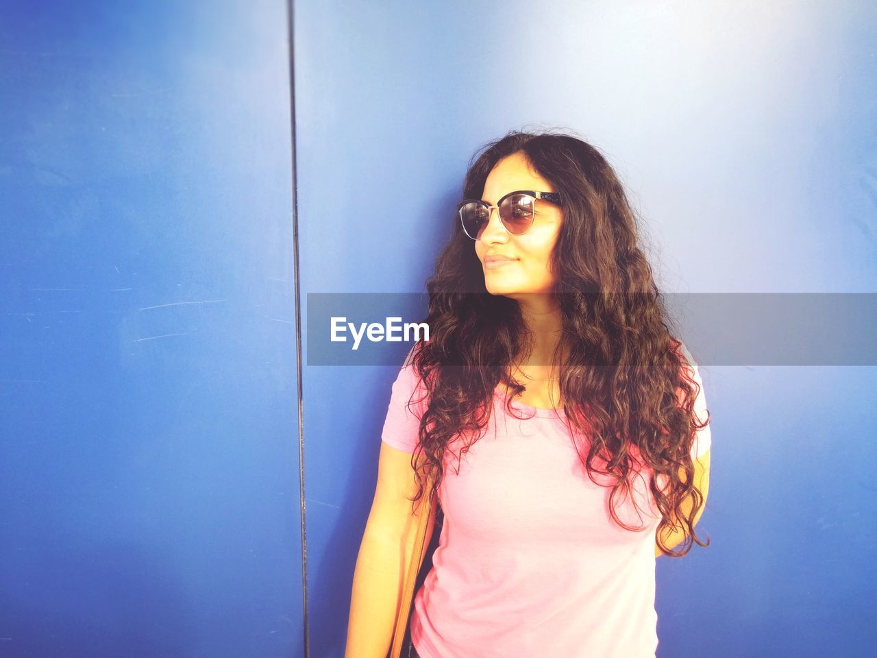 long hair, fashion, one person, hairstyle, blue, young adult, sunglasses, adult, women, glasses, red, portrait, copy space, brown hair, photo shoot, waist up, casual clothing, standing, singing, arts culture and entertainment, lifestyles, smiling, cool attitude, nature, looking at camera, person, looking, curly hair, indoors, sunlight, happiness, emotion, teenager, female, architecture