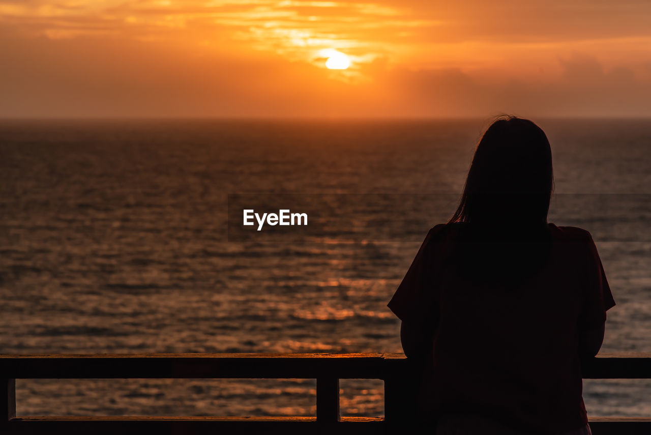 REAR VIEW OF SILHOUETTE MAN LOOKING AT SEA AGAINST SKY DURING SUNSET