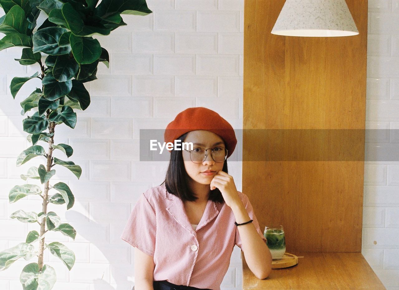 Portrait of young woman sitting at table against wall