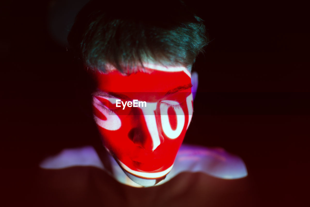 Close-up of shirtless man with light on face against black background