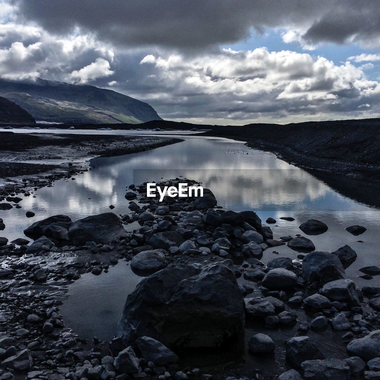 Rocks in river against cloudy sky